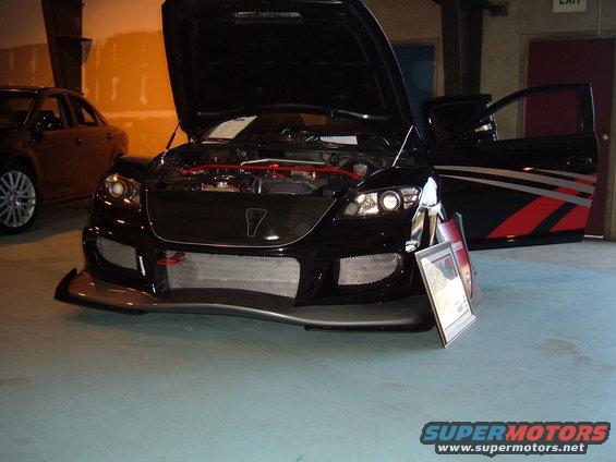 Black sports car with hood and door open, showing engine and custom graphics on the door. Another car is visible to the left