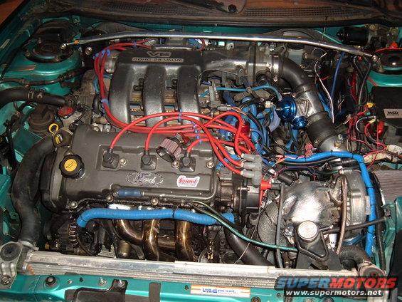 Engine bay with V6 DOHC 24 valve engine, red spark plug wires, blue hoses, and turbocharger