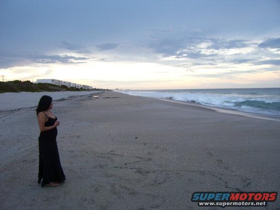 Woman in black dress on beach with ocean and buildings in background