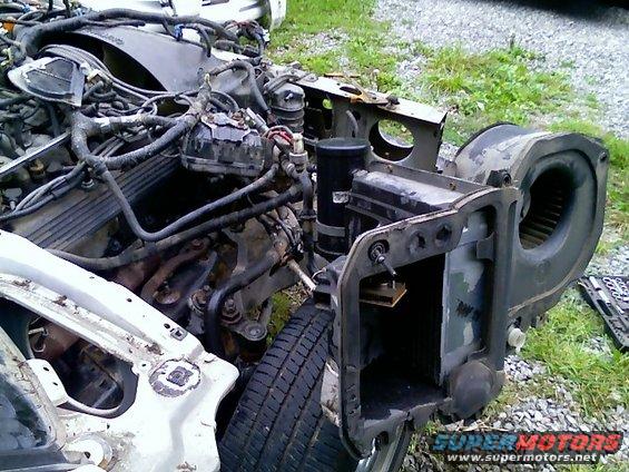 Disassembled car engine, radiator support, and HVAC blower motor housing. Wires and hoses are disconnected