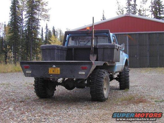 Blue flatbed truck with large tires and a shovel in the bed