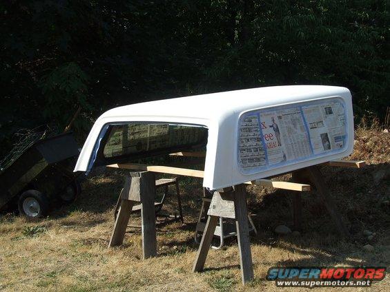 white truck bed cap on sawhorses, newspaper taped to windows