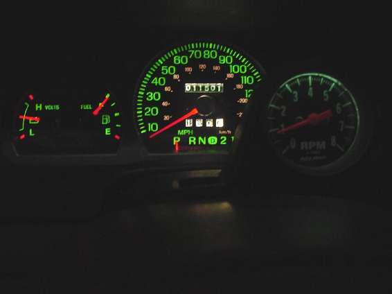 Vehicle dashboard with lit green gauges including speedometer, fuel, volts, and RPM. Odometer reads 011501