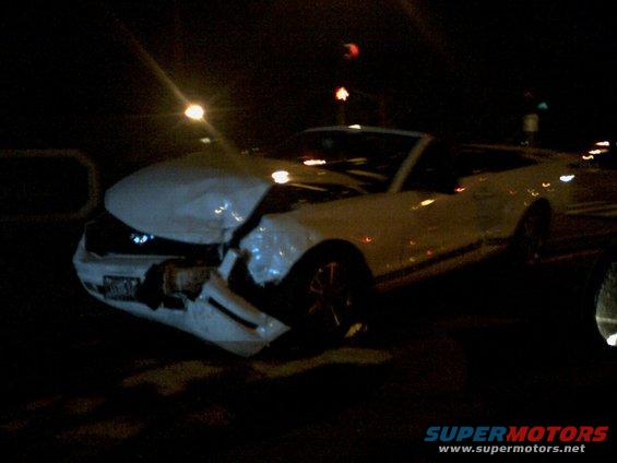 White convertible sports car with heavily damaged front end, seen at night
