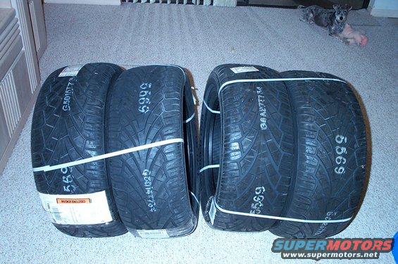 Four new tires stacked in pairs, bound with white straps. White numbers '5699' and '6999' are visible on the sidewalls