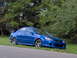 2003 Mazda Protege - A blue 2003 Mazda Protege sedan is parked on the side of the road with trees in the background.