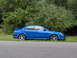 2003 Mazda Protege - This blue 2003 Mazda Protege sedan, equipped with a rear spoiler, is captured in a side profile view parked beside a paved road.