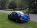 2003 Mazda Protege - Rear view of a blue 2003 Mazda Protege sedan with a spoiler, parked on the side of a road.