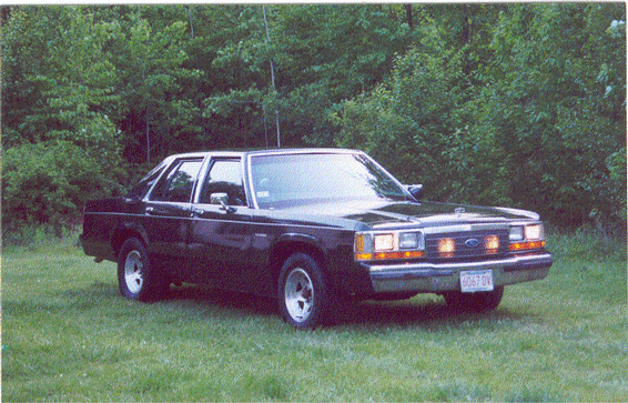 1988 Ford Crown Victoria parked on grass with trees in background