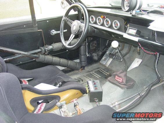 Interior of a race car with racing seats, roll cage, and gauges on the dash