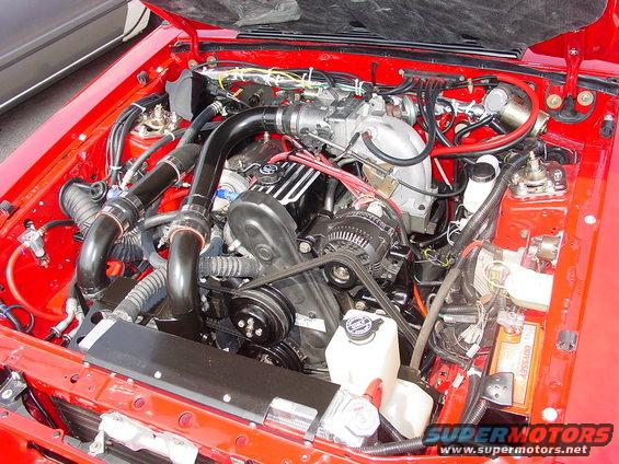 Engine bay with V8 engine, black intake tubes, and red fender wells. Odyssey battery visible