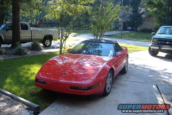 Red convertible sports car parked in a driveway with two trucks nearby