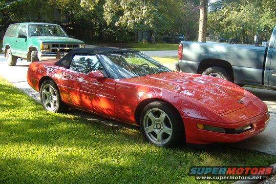 1994 Chevrolet Corvette convertible parked on grass next to a green SUV and a gray pickup truck