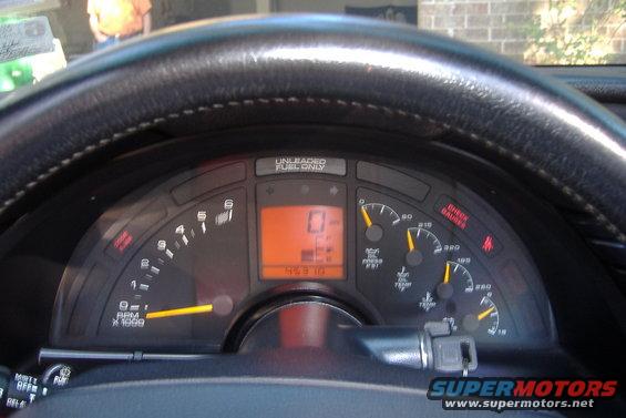 Dashboard gauges and steering wheel of a car. Digital odometer shows 0 miles
