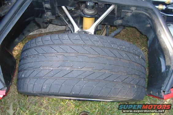 Close-up of a car's front wheel and suspension system. The tire is worn