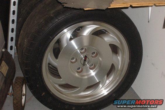 Close-up of a 1994 Chevrolet Corvette wheel with a tire. The center cap has a checkered flag and a red emblem
