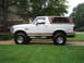 1996 Ford Bronco - Side profile of a white 1996 Ford Bronco a tan soft top and lifted suspension.