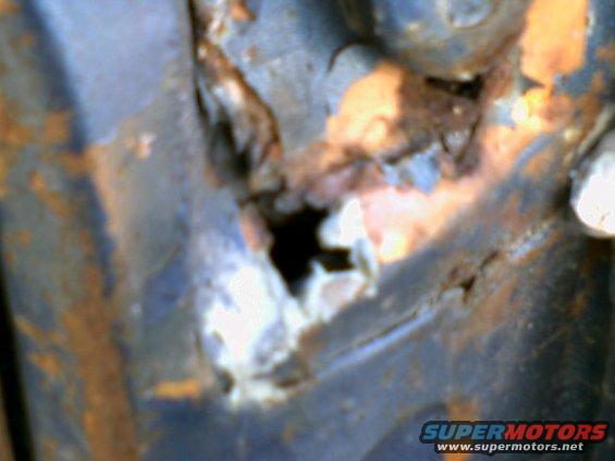 Close-up of heavily rusted metal with a large hole, showing orange and blue tones