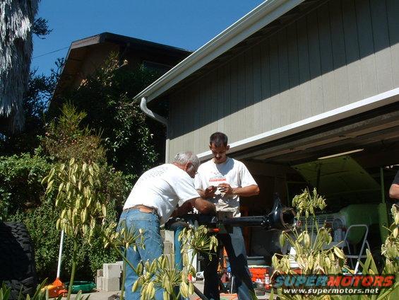 1994 Jeep YJ axle assembly being worked on by two men outdoors near a garage