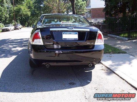 Black Ford Fusion sedan parked on a street, rear view. Two other cars are visible in the background
