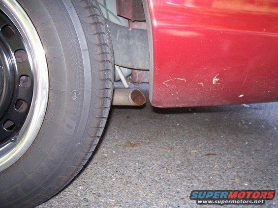 Close-up of a red car's rear quarter panel, showing some scuffs, next to a tire and exhaust pipe