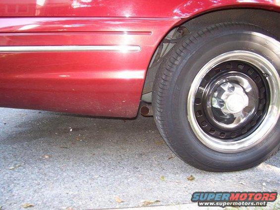 Red car side view, showing lower body panel with chrome trim and a black steel wheel with a chrome lip