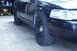 1999 Ford Crown Victoria - Front passenger side view of a black sedan with steel wheels and a visible headlight assembly.