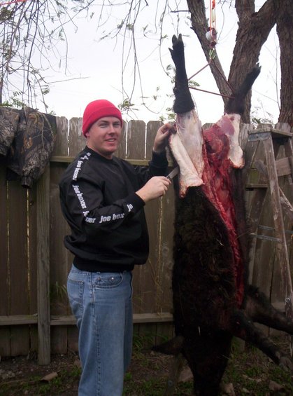 Man in red hat butchering hanging animal