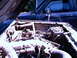 1987 Ford Bronco II - The engine bay of a 1987 Ford Bronco II, dual batteries and a glimpse of another vehicle behind it.