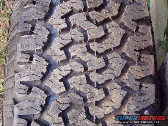 Close-up of a worn off-road tire tread with aggressive block pattern. Text 'SUPERMOTORS www.supermotors.net' visible