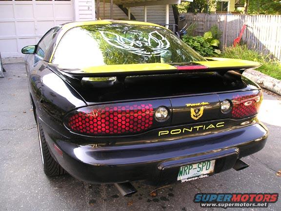 Black Pontiac Trans Am with yellow accents, rear view. Honeycomb taillights and a spoiler are visible