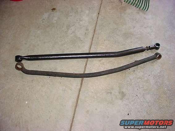 Two steering linkage bars, one black and one rusty, laid on a concrete floor