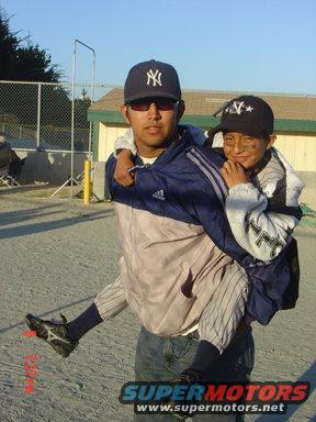 Man with New York Yankees cap gives a piggyback ride to a child wearing a similar cap