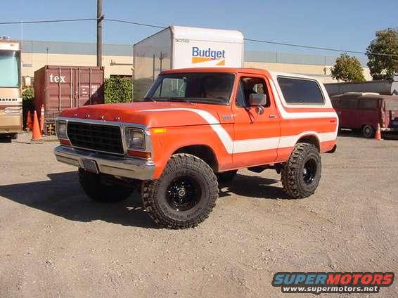 Orange and white Ford Bronco with black off-road tires, parked on gravel