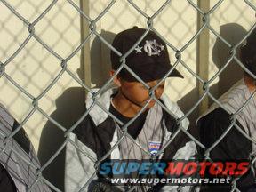 Child in baseball uniform and cap behind chain-link fence