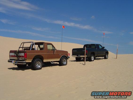 Brown 1991 Ford Bronco and dark green Dodge Ram on sand dunes