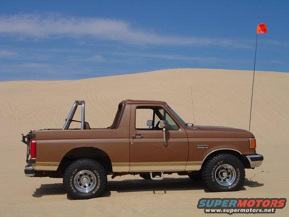 1991 Ford Bronco parked on sand dunes with an orange flag on a pole