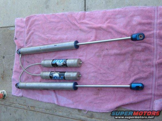 Four Fox shock absorbers with blue end caps laid out on a pink towel