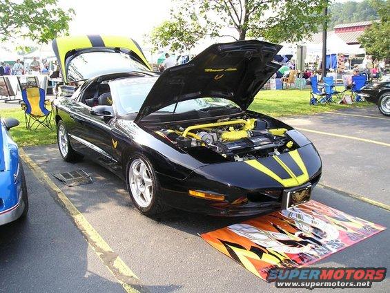 Black 1994 Pontiac Trans Am with yellow racing stripes, hoods open, parked at a car show