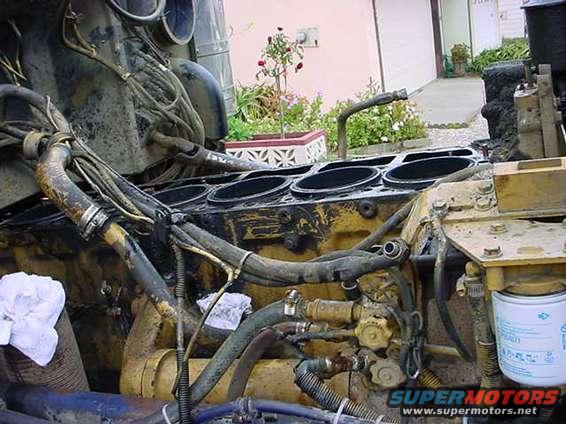 Engine block with cylinders exposed, hoses and wires attached. A white oil filter is visible on the right