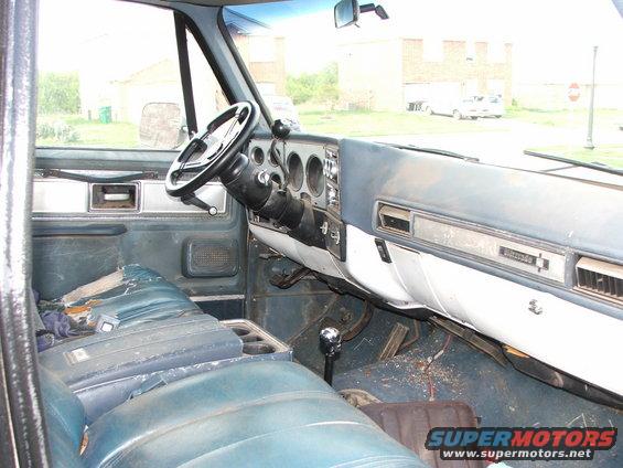 1980 Chevrolet Blazer interior showing ripped blue bench seat, dashboard, steering wheel, and floor shifter