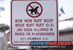sign with dog silhouette in red circle with slash, text says 'BOW WOW RUFF WOOF WOOF RUFF RUFF 12-51 (NO DOGS ALLOWED IN PARKS OR PLAYGROUNDS) CITY ORDINANCE 12-51 DOG OFFICER'