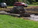 1979 Ford Bronco - Several vehicles navigate a muddy off-road course with trees and grass surrounding the area.