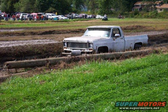 White pickup truck stuck in mud, front grille visible, side view
