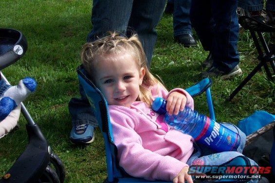 Young girl in a blue camping chair holding a bottle of Propel water. She wears a pink sweatshirt and has blonde hair in pigtails