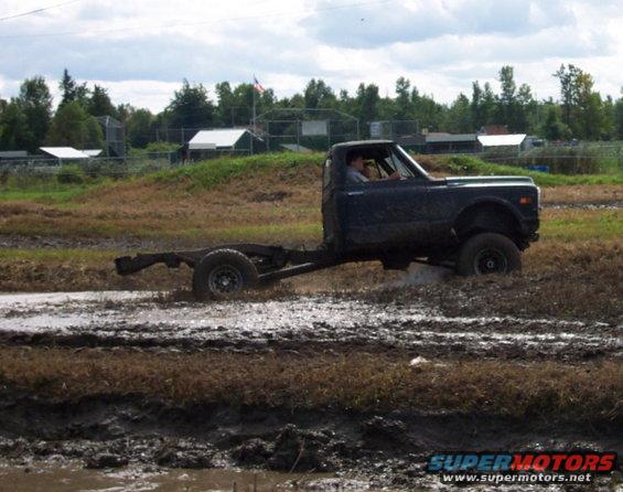 Dark pickup truck chassis with a driver navigating through a muddy field