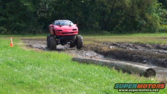 Red monster truck with oversized tires driving through a muddy track with a log obstacle