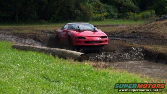 Red sports car navigating a muddy obstacle course