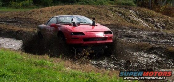Red car with snorkel exhaust pipes driving through mud pit