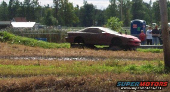 Red sports car with missing wheels stuck in mud